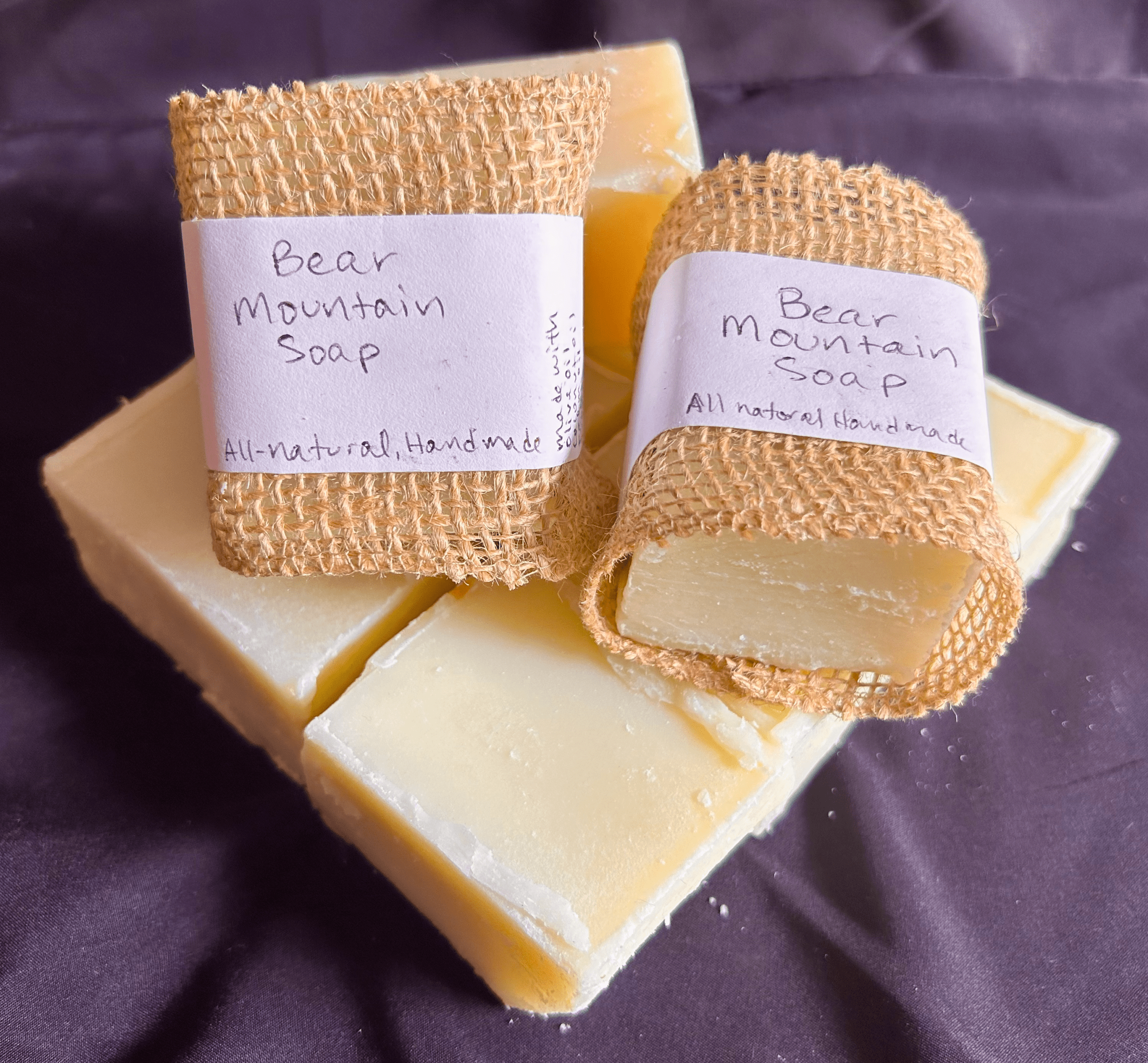 Handmade soap bars labeled "Bear Mountain Soap" wrapped in burlap on a dark fabric